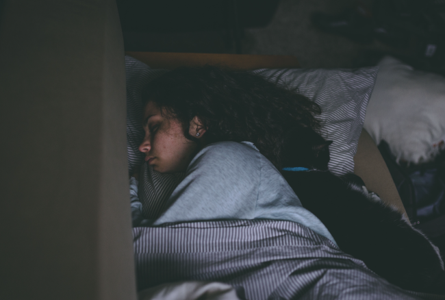 Young woman sleeps under covers in a darkened room.